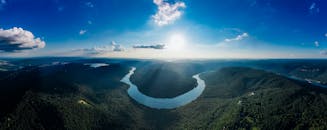 在明亮的蓝天下，群山环绕着郁郁葱葱的河流，其弯曲的形态构成了一幅令人惊叹的鸟瞰图