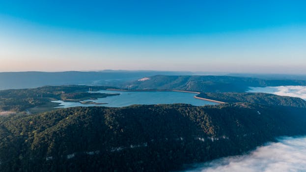 Stunning aerial view of a serene mountain reservoir surrounded by lush forests and misty skies.