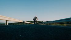 在天空晴朗的开放高速公路上，一名摩托车手骑行着，展现出冒险与自由