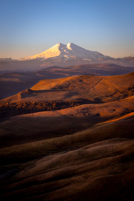 A stunning view of a snow-capped mountain with golden hills at sunrise.