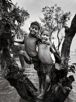 Two boys having fun on a tree in a flooded area, embodying happiness and resilience.