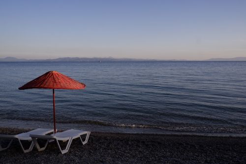 Free Serene beach scene in Muğla, Türkiye with empty loungers and a red parasol during a calm afternoon. Stock Photo