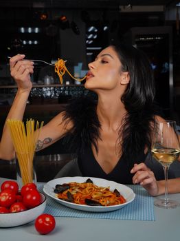Woman enjoying spaghetti with seafood and a glass of white wine.