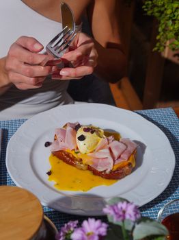 Tasty eggs benedict with ham in a sunny outdoor brunch setting.