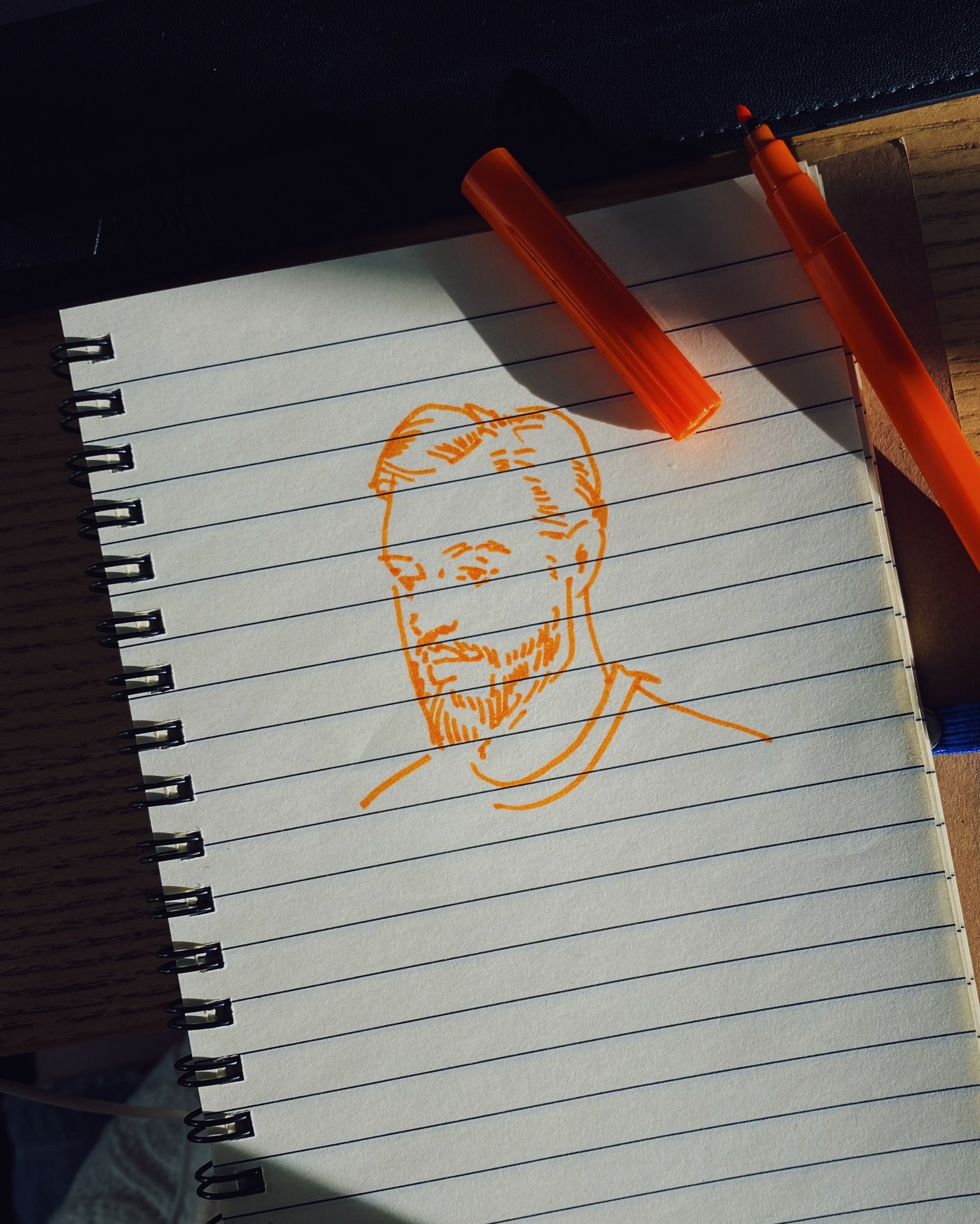Artistic sketch of a man's face on lined notebook paper with orange pen.