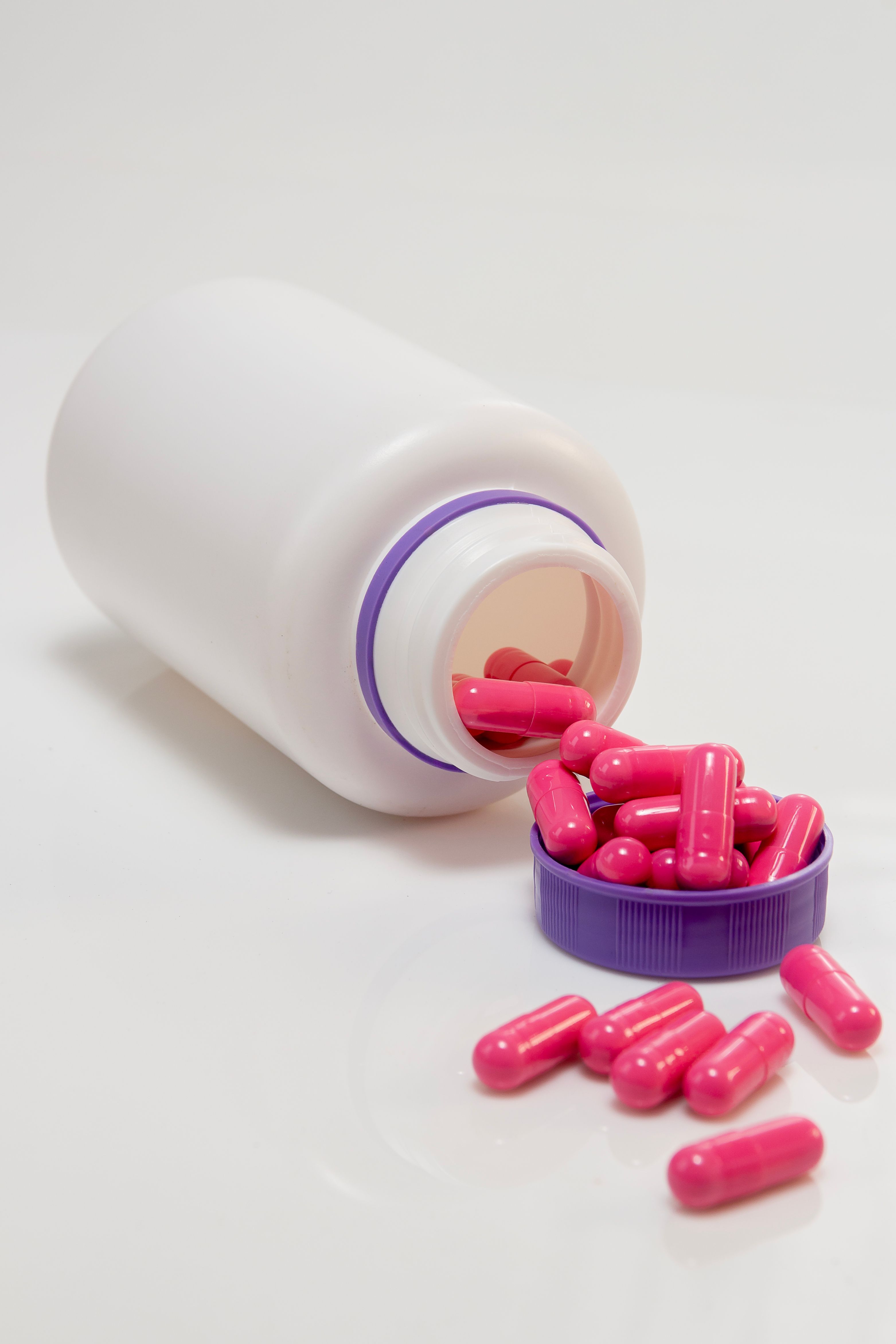 Pink Capsules Beside Plastic Bottle on a Surface · Free Stock Photo