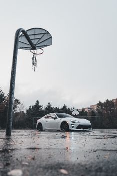 A white sports car parked on an empty wet basketball court during a rainy day.