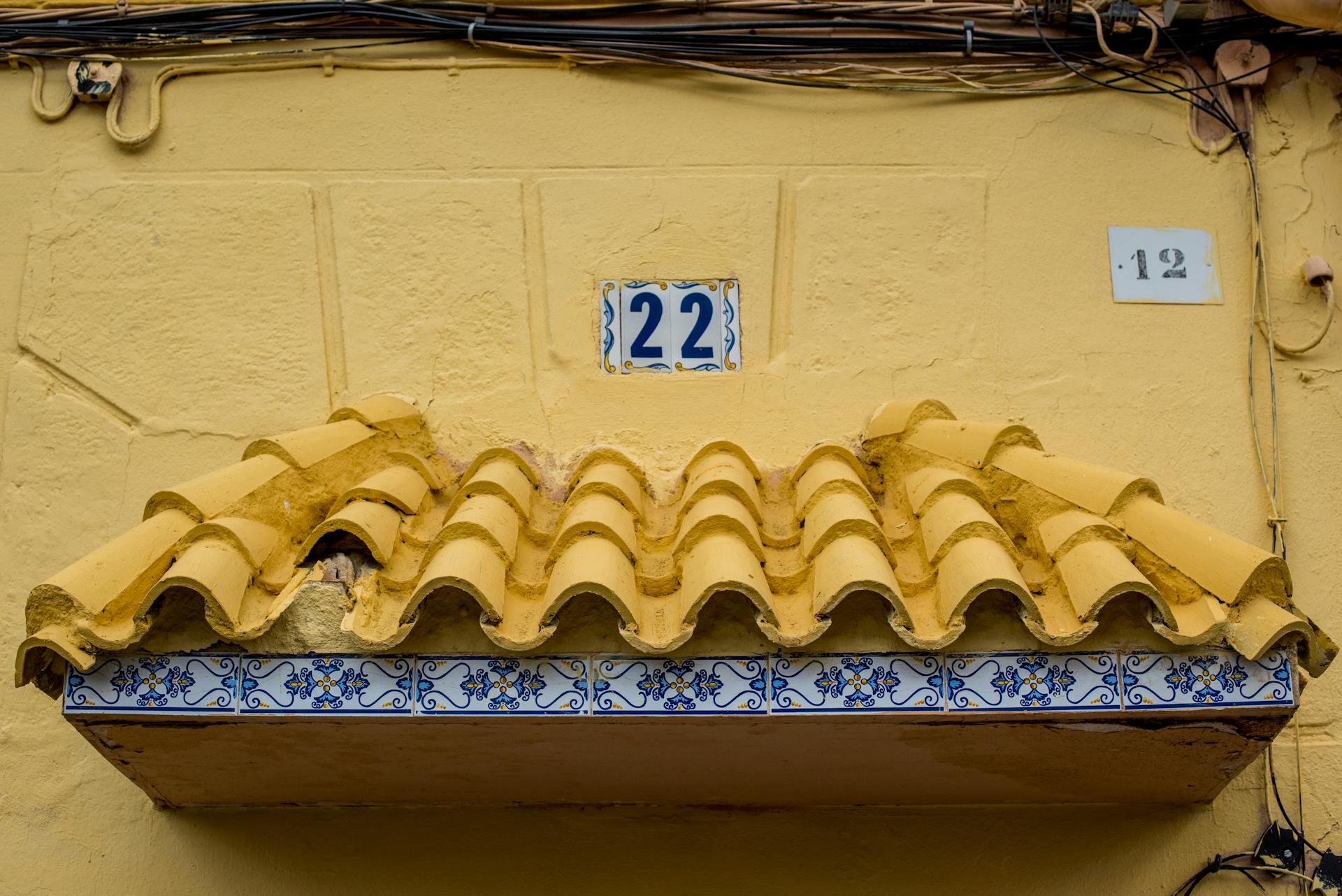 Yellow stucco façade with traditional tiles and house number 22, capturing rustic architectural charm.
