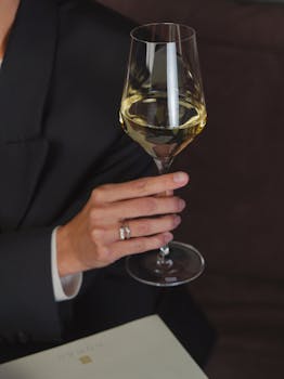 Close-up of hand holding a glass of white wine with stylish attire.