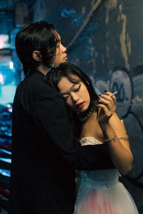 Free Young couple in an intimate embrace in a dimly lit urban alley, creating a moody atmosphere. Stock Photo