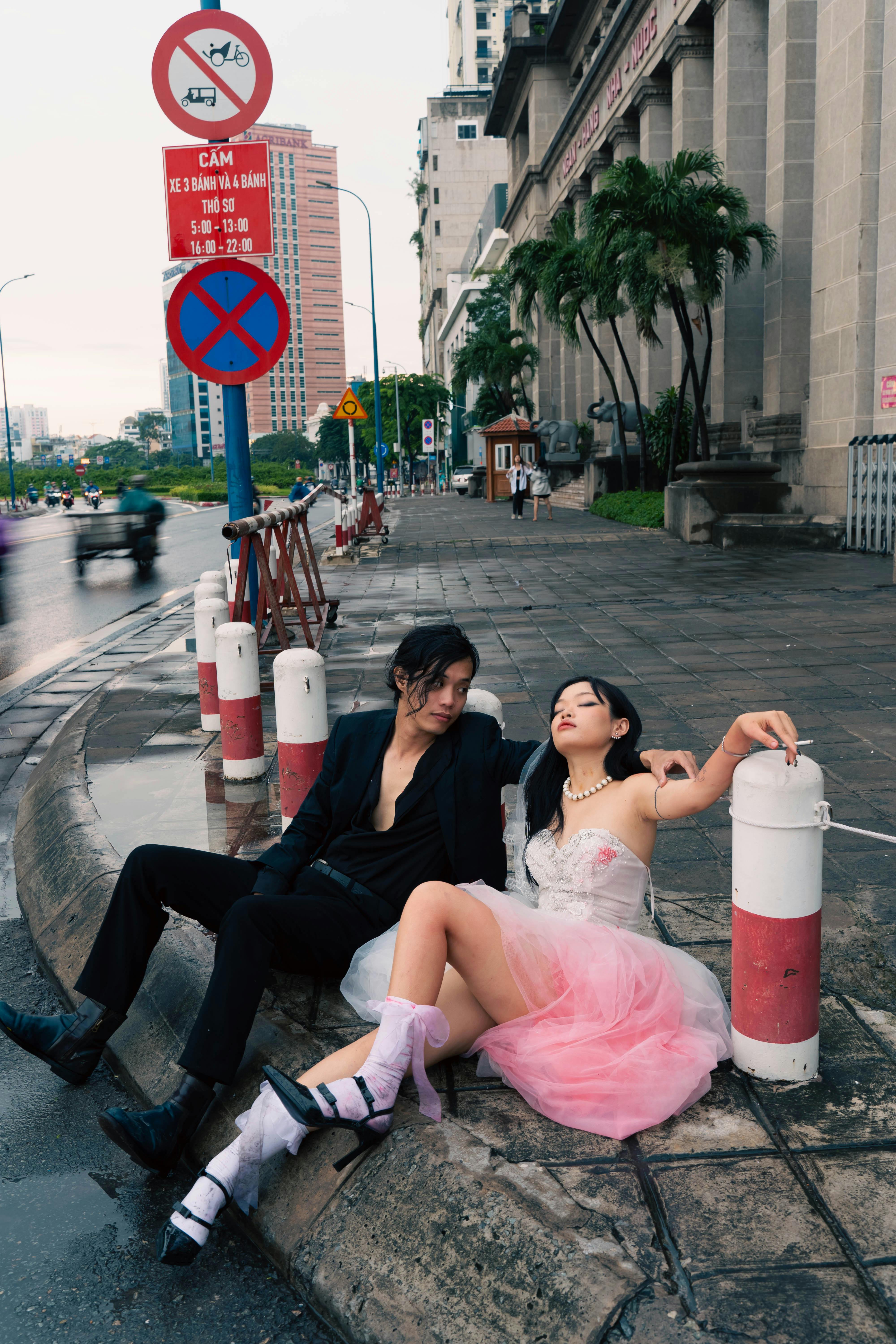 Couple resting on city street curb, showcasing urban style and mood.