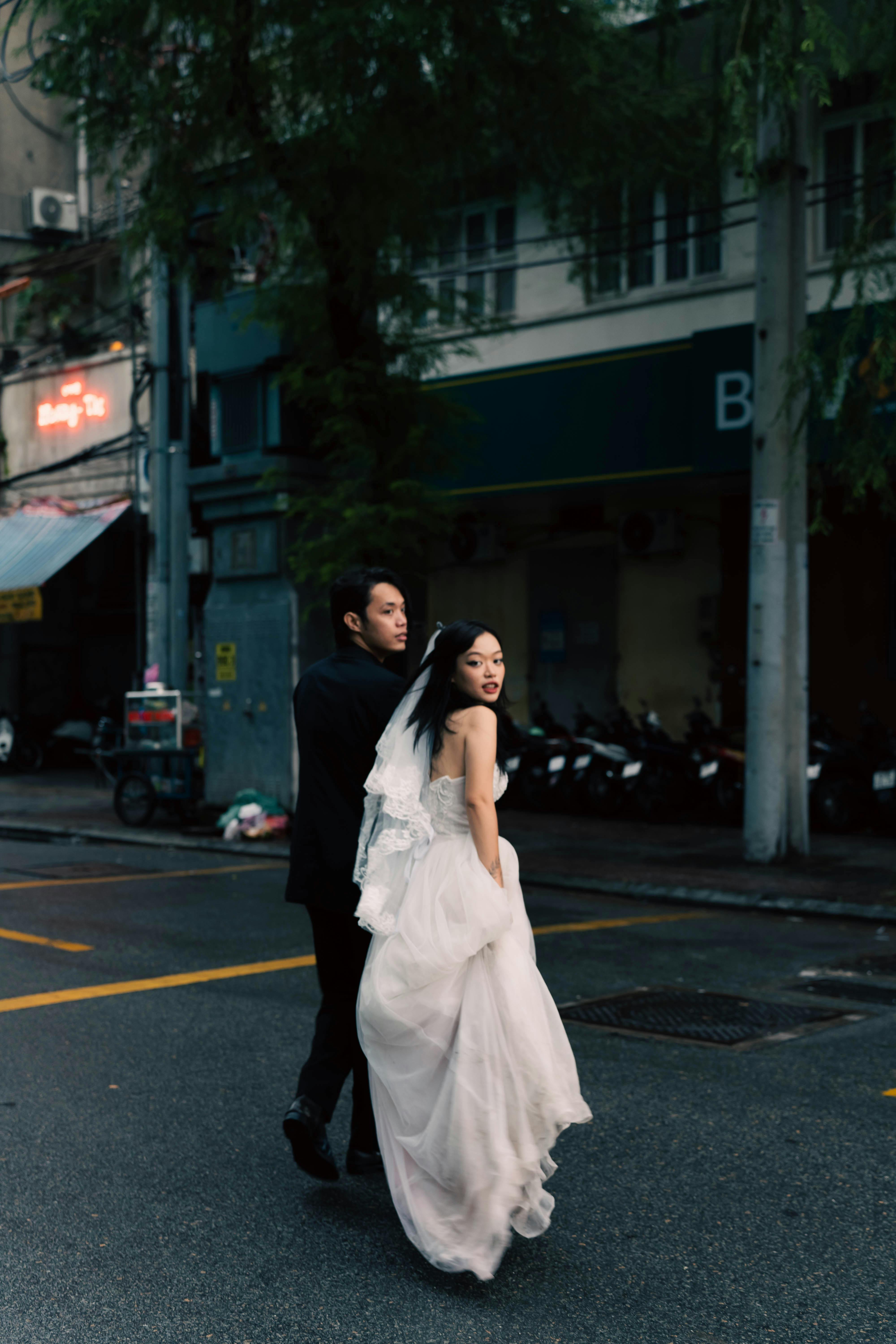 A bride and groom cross the street with an urban backdrop, capturing a romantic and modern city vibe.
