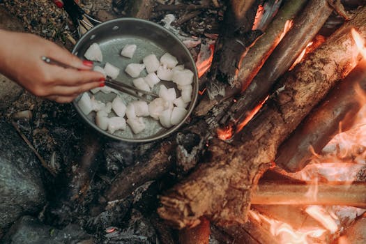 Close-up of fish being cooked over an open flame using chopsticks, outdoors.
