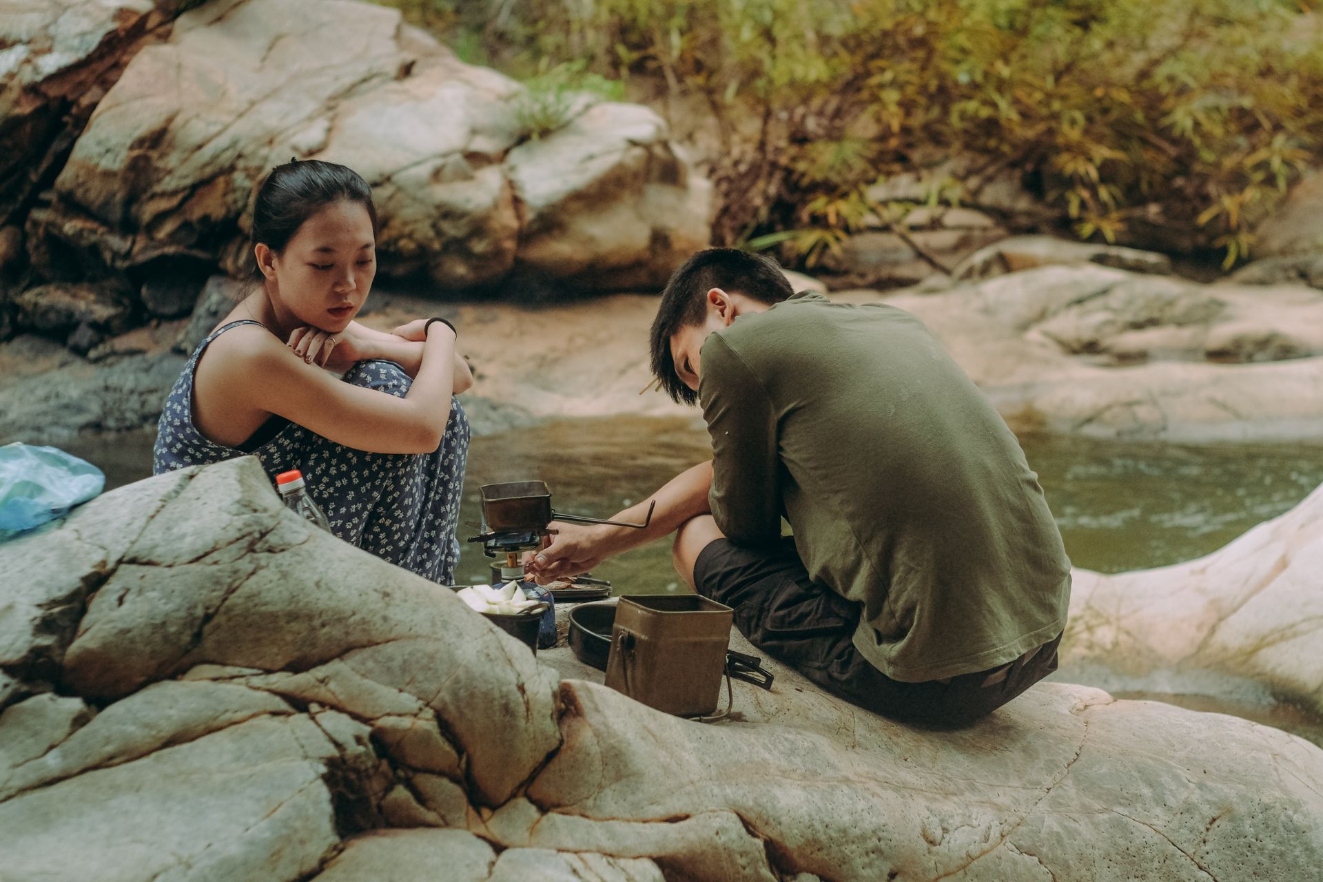 A young couple enjoys outdoor cooking while camping by the scenic river.