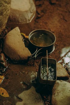 Cooking pots in a natural stream area, surrounded by rocks and water, creating a rustic outdoor atmosphere.