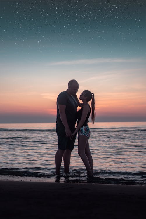 Free Romantic Couple Standing on Seashore Under Night Sky Stock Photo