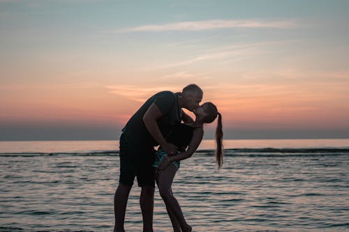 日没時に水域を横切ってキスする男と女