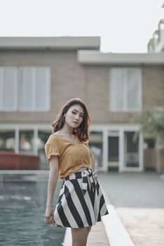 Stylish young woman in a chic outfit posing beside a pool in an outdoor setting.