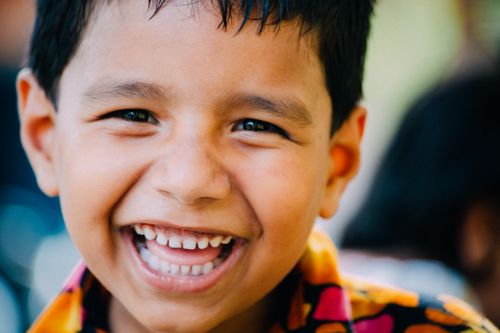 Free A joyful child with a big smile wearing a colorful shirt, captured outdoors in natural light. Stock Photo