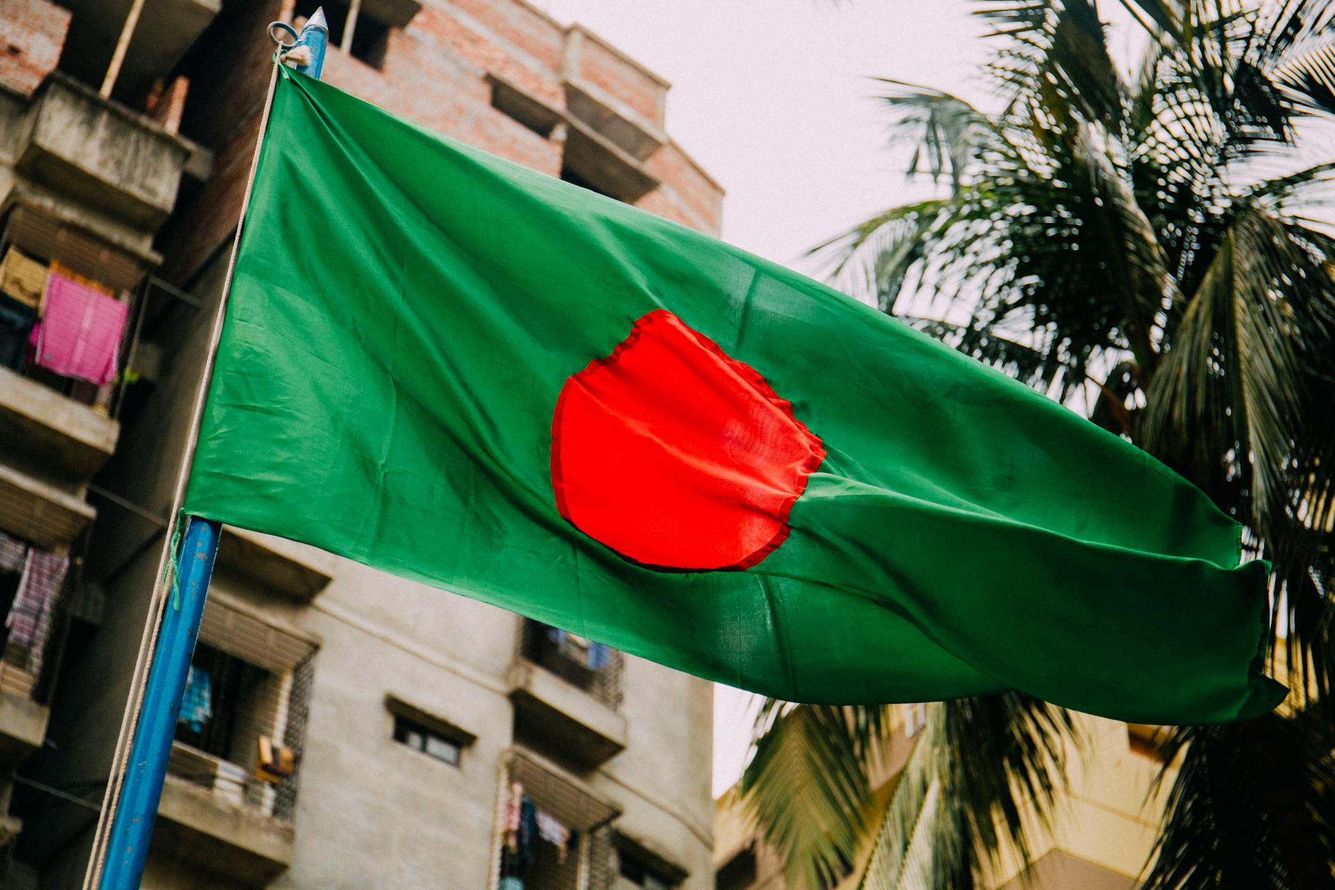 A vibrant Bangladesh flag waving against a cityscape backdrop, evoking patriotism.