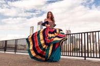 一名女子身穿色彩缤纷的传统服装，在城市河滨旁以摩天大楼为背景摆姿势