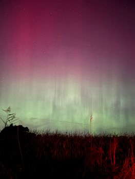 Captivating view of aurora borealis lighting up the night sky over dark silhouetted landscape.