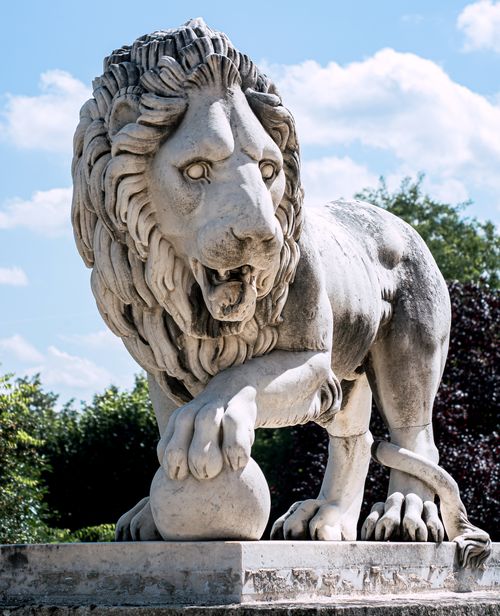 Free A detailed stone lion statue standing regally in an outdoor park setting under a bright sky. Stock Photo