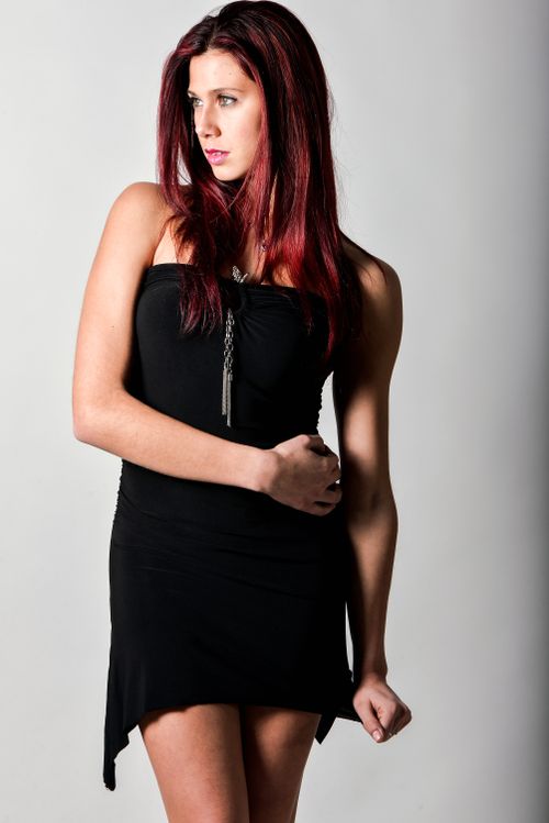 Free Stylish woman with red hair in a black dress posing confidently. Stock Photo