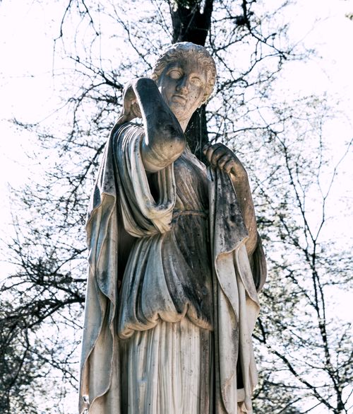 Free Elegant ancient Greek-style marble statue outdoors surrounded by trees. Stock Photo