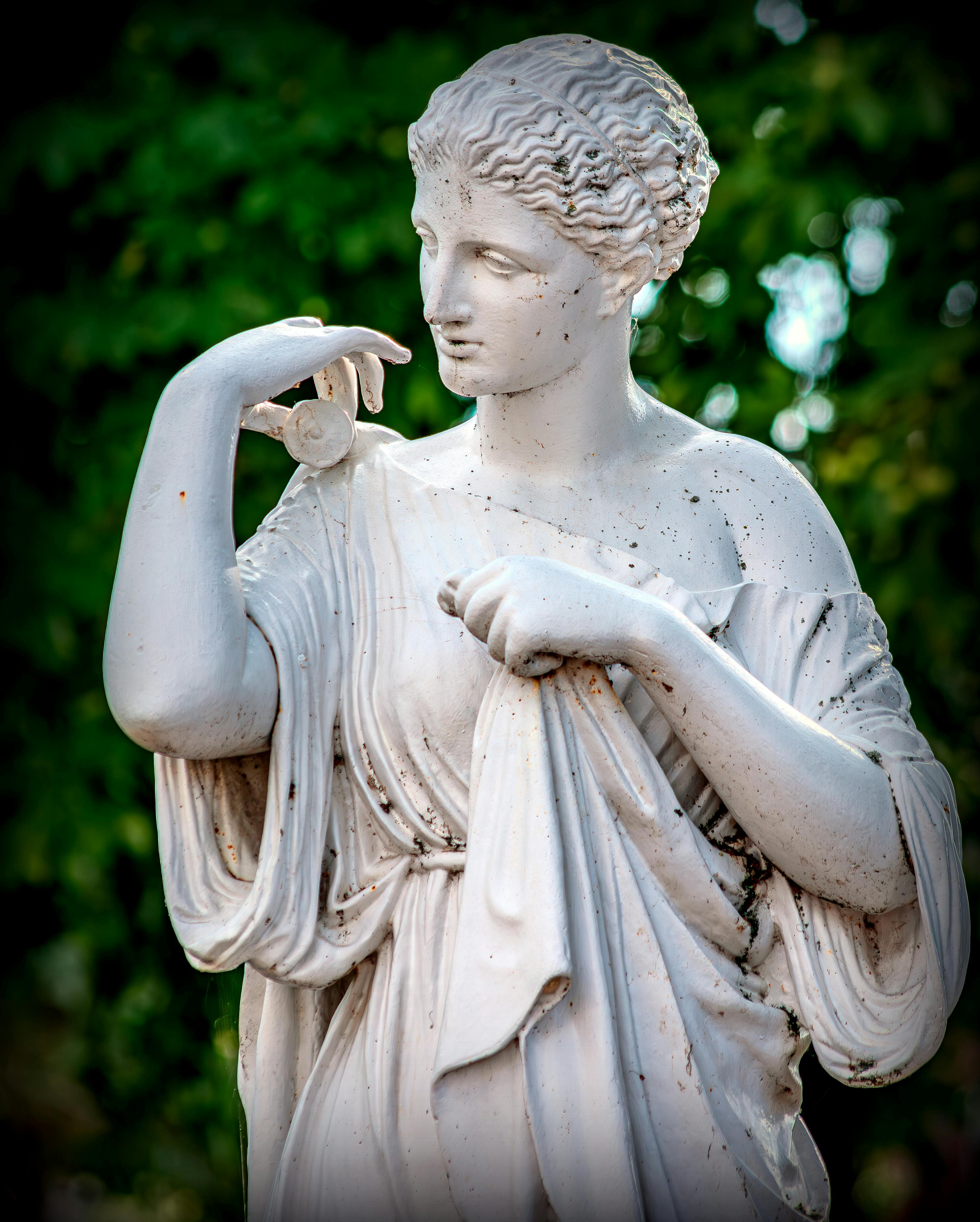 A classic marble statue of a woman set against lush greenery.