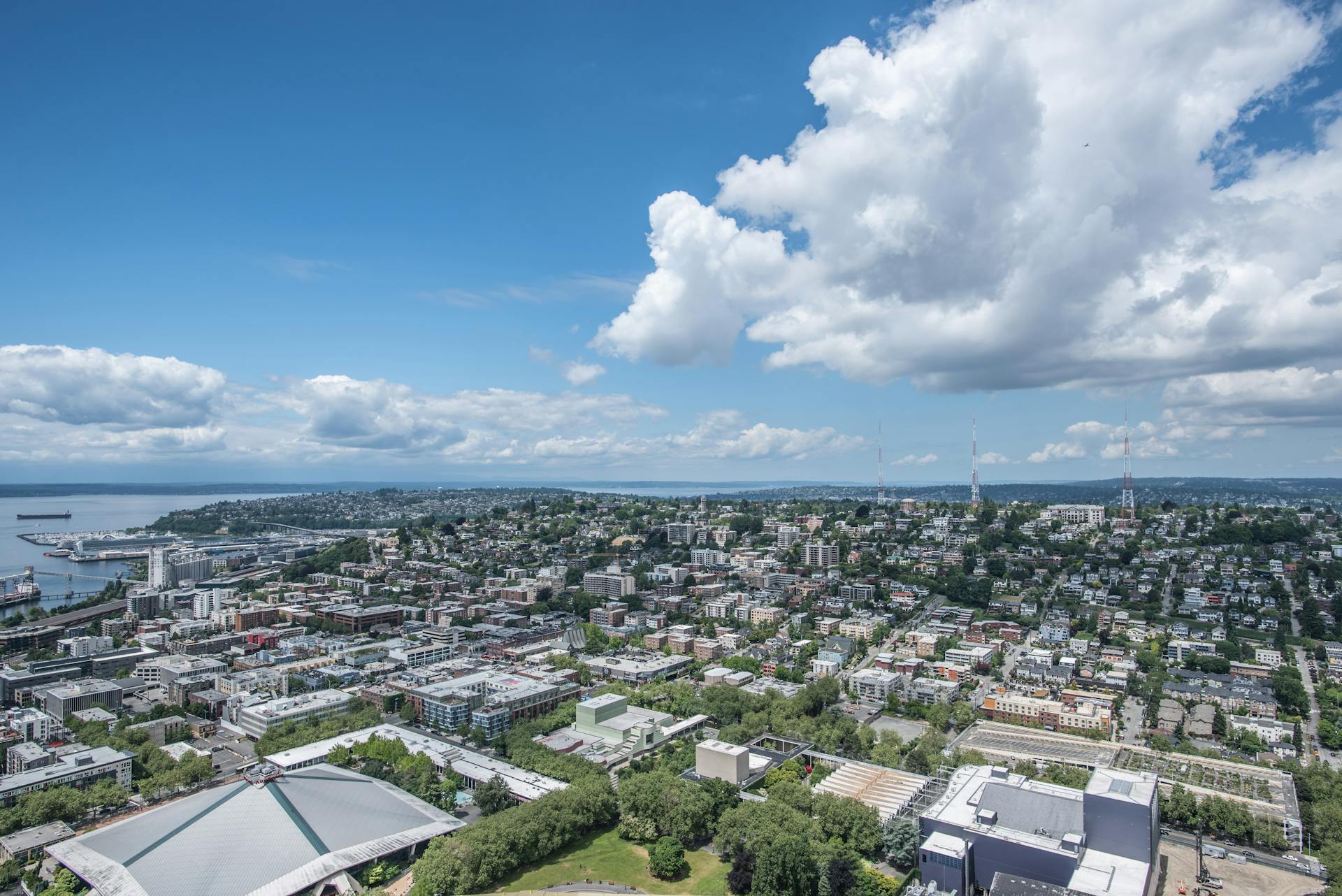 Aerial city view of Seattle overlooking buildings, Elliott Bay, under blue sky with clouds.