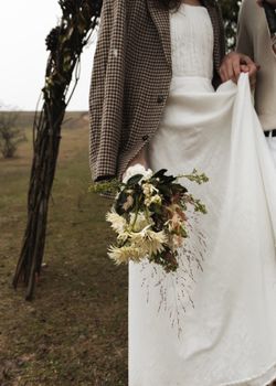 A close-up of newlyweds holding hands outdoors, showcasing bridal attire and bouquet.