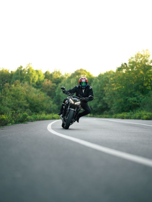 Free Motorcyclist taking a sharp turn on a scenic forest road, wearing full gear and helmet. Stock Photo
