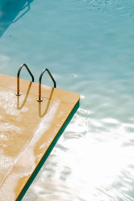 Bright sunny day by the poolside with clear shimmering water and metal ladder.