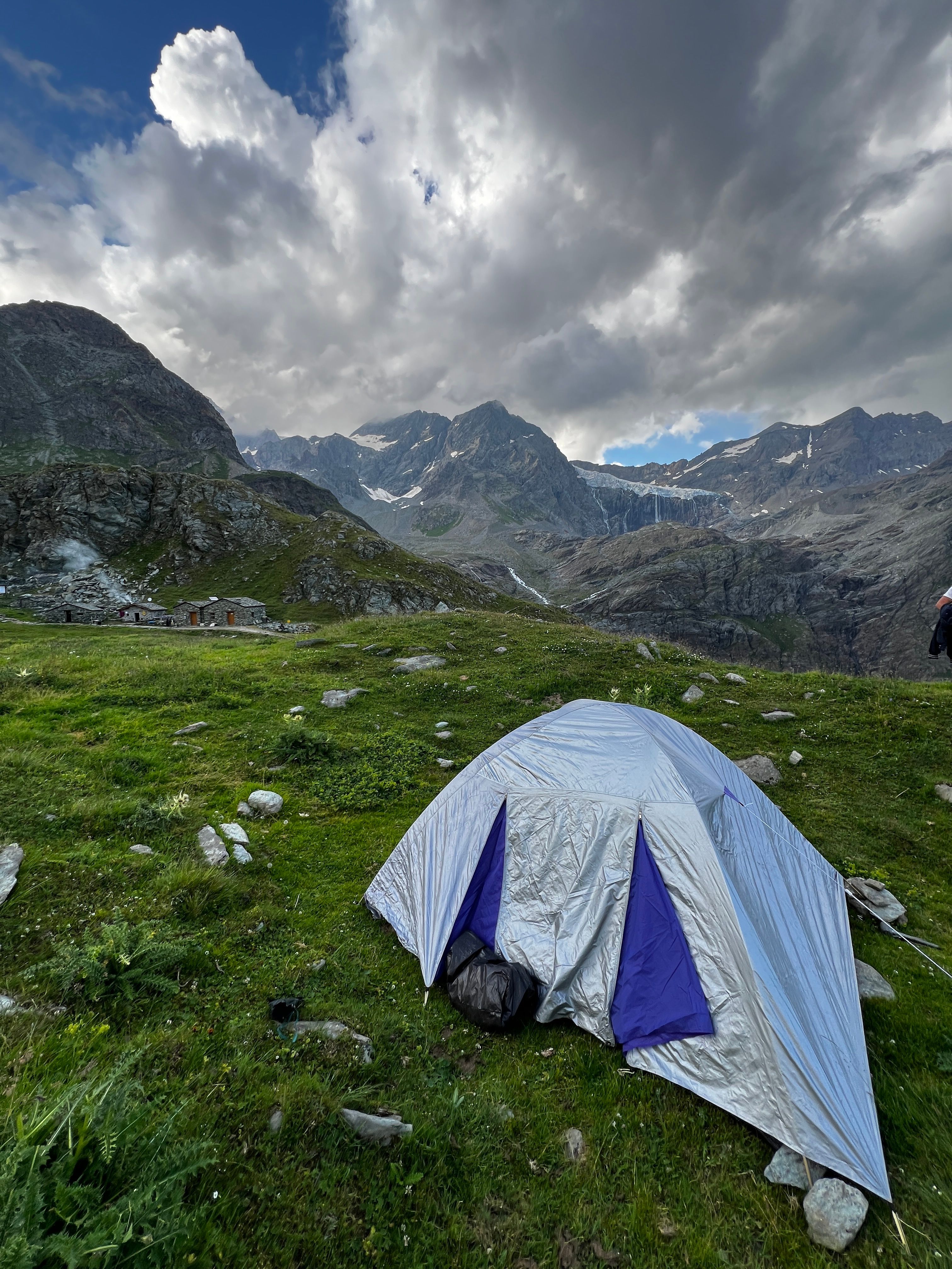 Tent setup in lush mountain scenery under dramatic clouds.