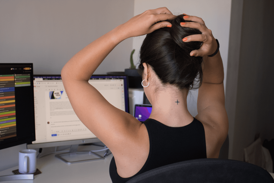 Una mujer con un tatuaje sostiene su cabello en un espacio de trabajo moderno con dos pantallas.