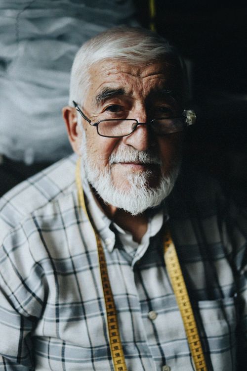 Free Elderly tailor wearing glasses and measuring tape, smiling. Stock Photo