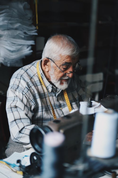 Free Senior man sewing in a workshop with sewing machine and measuring tape. Stock Photo