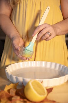 Woman preparing pie crust with baking dish and lemon in a cozy kitchen.