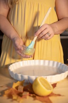 Woman preparing pie crust with brush and lemon in an autumn kitchen setting.