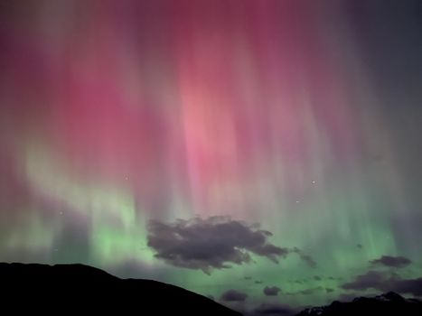 Vibrant red and green aurora borealis illuminating the night sky with clouds and silhouettes.