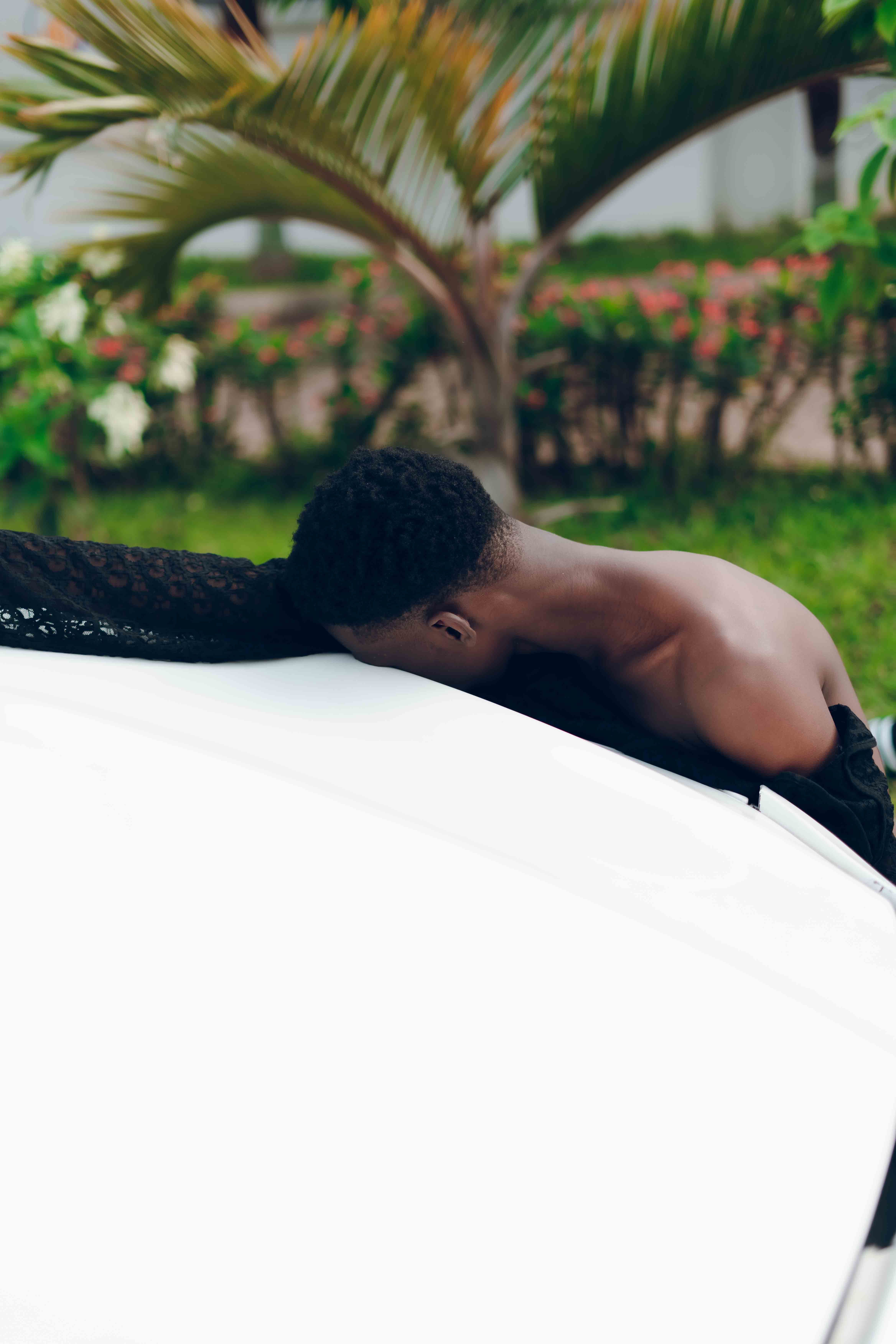 A creative outdoor portrait of a black male model leaning on a sleek white car.