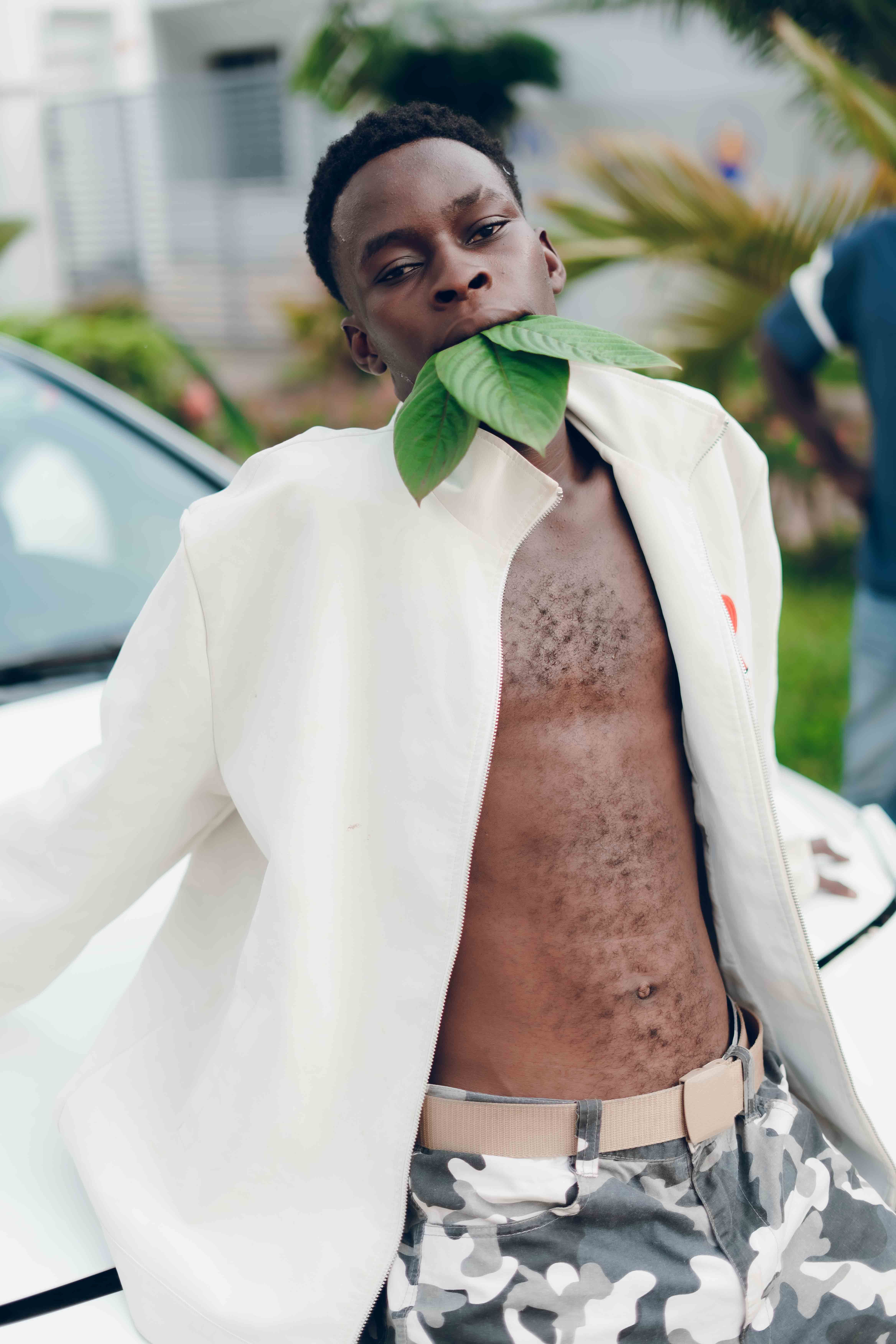 Artistic outdoor portrait of a young man with leaves in a playful pose in Nigeria.