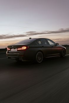 Luxury sedan cruising on a highway at twilight with a dramatic sky backdrop.