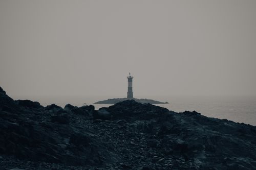 Free Solitary lighthouse on rocky coastline with misty sea view. Stock Photo