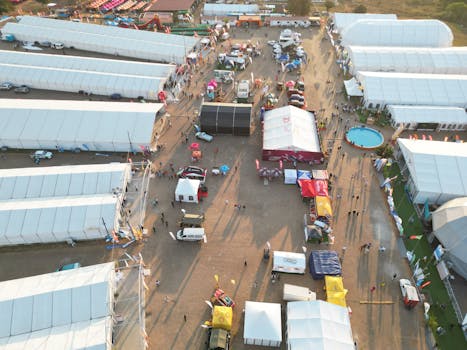 Bird's-eye view of a lively outdoor event with multiple white tents and people.