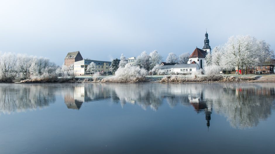 Frosty riverside scene with reflections of buildings and trees in Beverungen, Germany during winter.