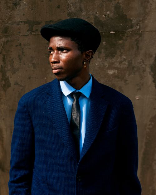 Free Portrait of a stylish man wearing a blue suit and black beret against a textured wall. Stock Photo