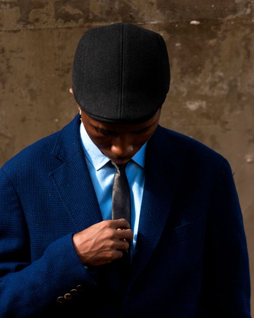 Free Man in blue suit and black cap adjusting tie. Street fashion moment. Stock Photo