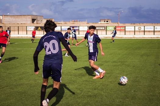 Youth soccer match on a sunny day, players engaged in action on green grass field.